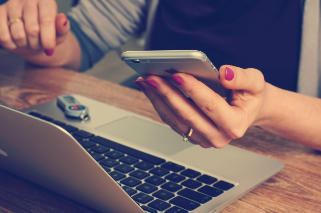 Woman holding iPhone and using laptop