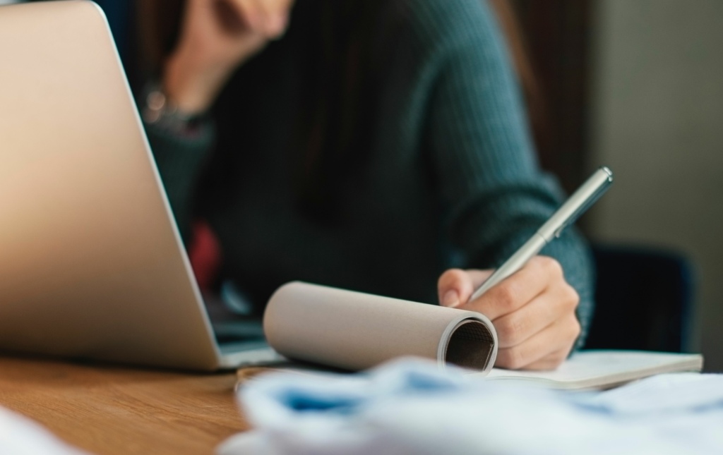 Woman writing in notebook and working at laptop