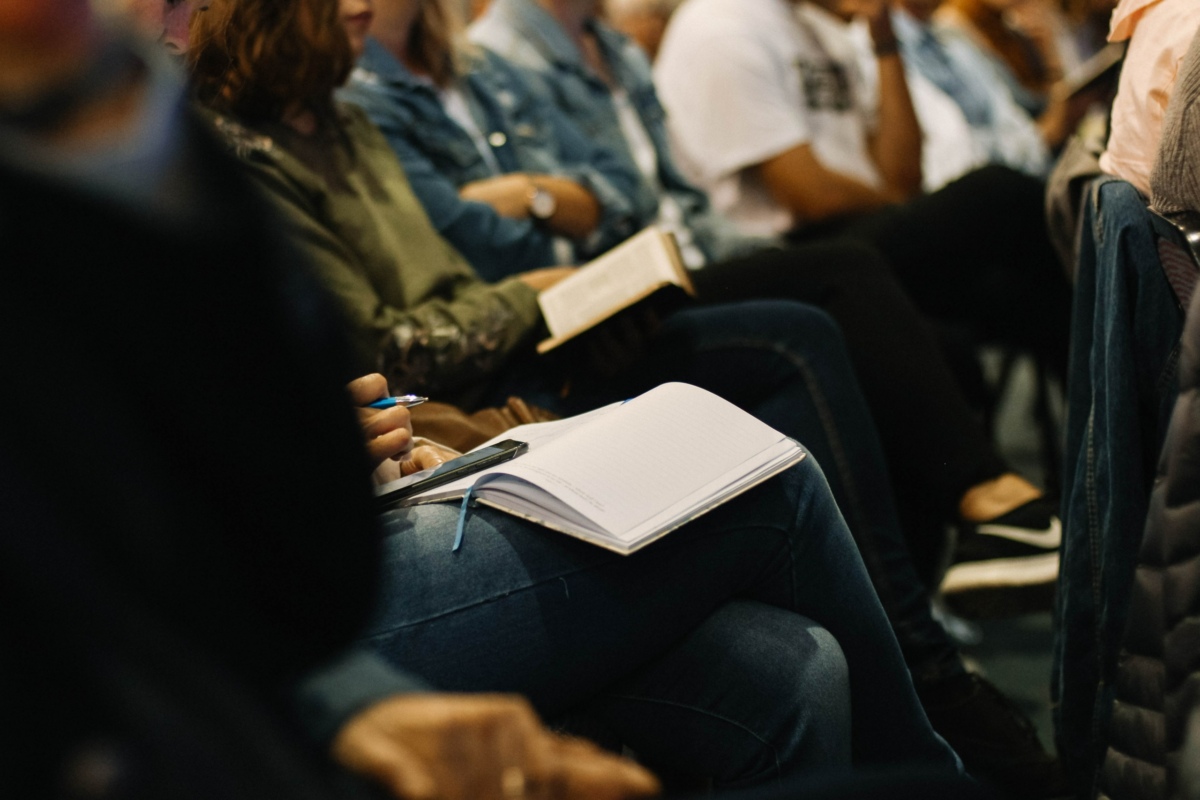 People sat in a row of chairs with notebooks on their laps